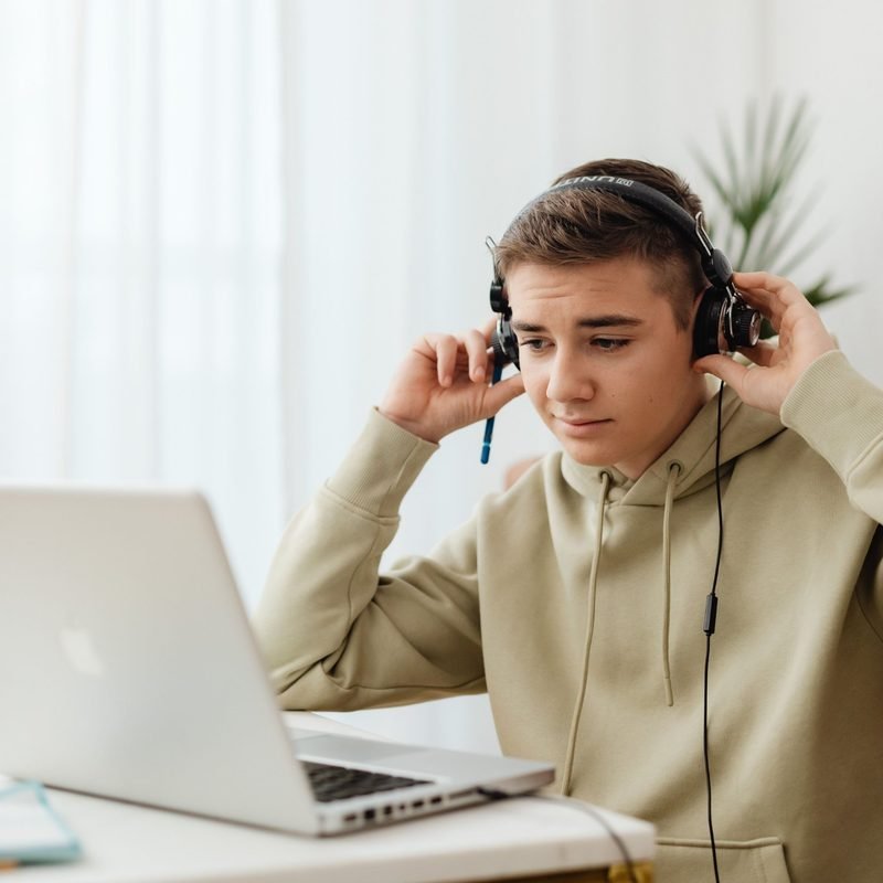 Teenager wearing headphones studying at a laptop at home