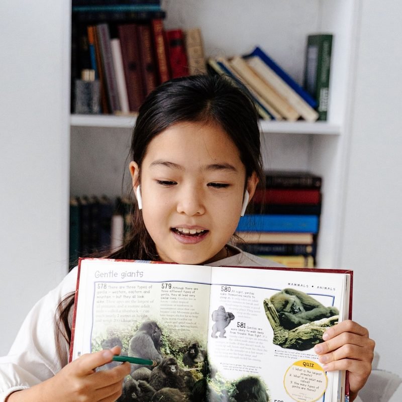 Girl showing an open book to her laptop during an online lesson